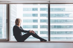 A woman sitting by the large window of a high rise.